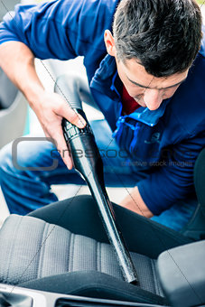 Young man using vacuum for cleaning the interior of a car