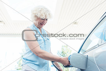 Active senior woman smiling while filling up the gas tank of her
