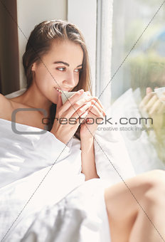 a woman sits on a windowsill with a cup of coffee