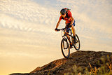 Cyclist in Red Riding the Bike Down the Rock at Sunset. Extreme Sport and Enduro Biking Concept.
