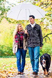 Woman and man having walk with dog in autumn rain