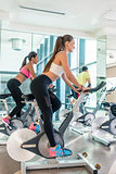 Fit women burning calories during indoor cycling class in a mode