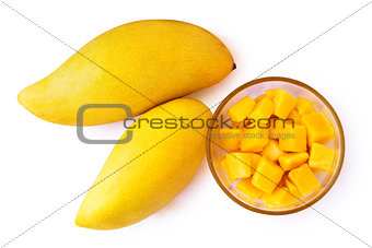 Two mango fruits and mango cubes on a plate.