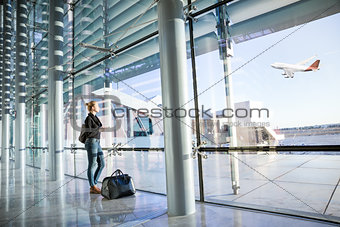 Young woman waiting at airport, looking through the gate window.