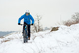Cyclist in Blue Riding Mountain Bike on Rocky Winter Hill Covered with Snow. Extreme Sport and Enduro Biking Concept.
