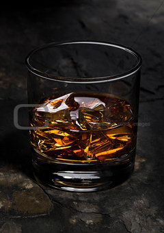 Elegant glass of whiskey with ice cubes on stone