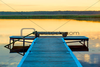 view of a wooden pier near a picturesque calm lake at dawn