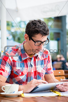Man drinking coffee in street cafe reading on tablet device