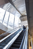 Businesswoman with large black bag and mobile phone ascending on escalator.