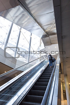 Businesswoman with large black bag and mobile phone ascending on escalator.
