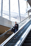 Businesswoman with large black bag and mobile phone descending on escalator.