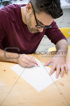 Young Designer Drawing the Sketch Using Pencil on the Wooden Table in Bright Studio