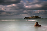 Stormy skies over Godrevy Lighthouse on Godrevy Island in St Ives Bay with the beach and rocks in foreground, Cornwall UK