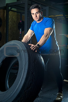 young strong athlete posing with a heavy wheel in the gym