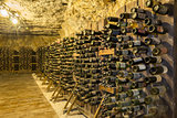 Many old wine bottles stacked on wooden racks in a cellar