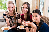Three young women eating cake indoors
