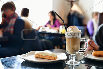 coffee with whipped cream and eclair on table in a cafe