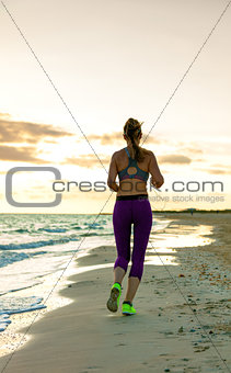 young woman in sport clothes on seashore at sunset jogging