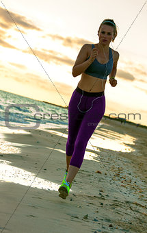 young woman in sport clothes on seacoast at sunset running