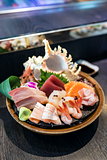 Selective focus decorated sashimi set in a bowl with ice and conch shell near the chef bar.