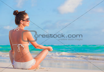 young girl in white bikini tanning at tropical beach