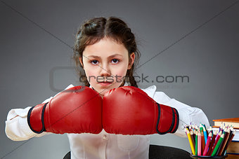 Playful cute little girl having fun in boxing gloves while leaning on grey background, selective focus