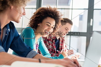 Cheerful woman writing an assignment while sitting between two classmates