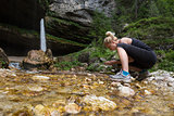 Active sporty woman drinking water from outdoor stream with her hands.