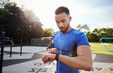 Young man at outdoor gym setting fitness app on smartwatch