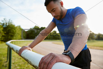 Male athlete leaning on fence at running track, close up