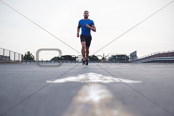 Male athlete running on a road towards camera, full length