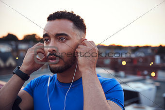 Male runner in urban setting adjusting earphones, close up