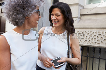 Two female work colleagues talking in the street, close up
