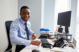 Young black man smiling to camera from his desk in an office