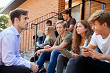 Teenage Students Talking To Teacher Outside School Buildings