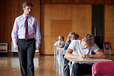 Teenage Students Sitting Examination With Teacher Invigilating