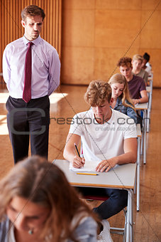 Teenage Students Sitting Examination With Teacher Invigilating