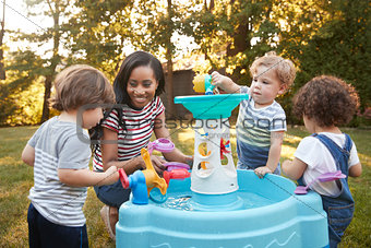 Mother And Young Children Playing With Water Table In Garden