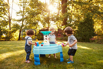 Group Of Young Children Playing With Water Table In Garden