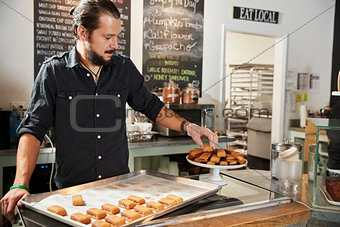 Waiter Behind Counter In Coffee Shop Arranging Cookie Display