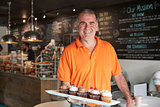 Portrait Of Male Owner With Tray Of Muffins In Coffee Shop