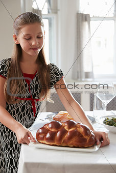 Girl puts challah bread on table for Shabbat meal, vertical