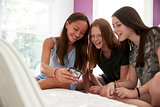 Three girlfriends on a bed using a smartphone, close up