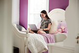 Teenage girl sitting on her bed using a laptop computer