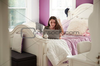 Teenage girl lying on her bed using a laptop computer