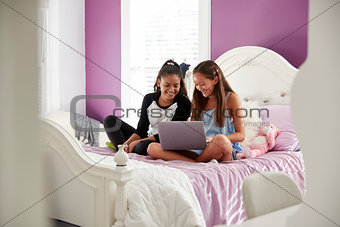 Two teen girls sitting on bed using laptop