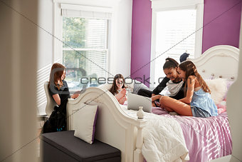 Four teen girls hang out using laptop and phones in bedroom