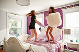Two teenage girls standing on a bed having a pillow fight
