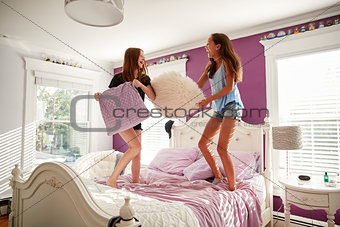 Two teenage girls standing on a bed having a pillow fight