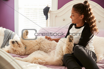 Young teen girl stroking pet dog on her bed